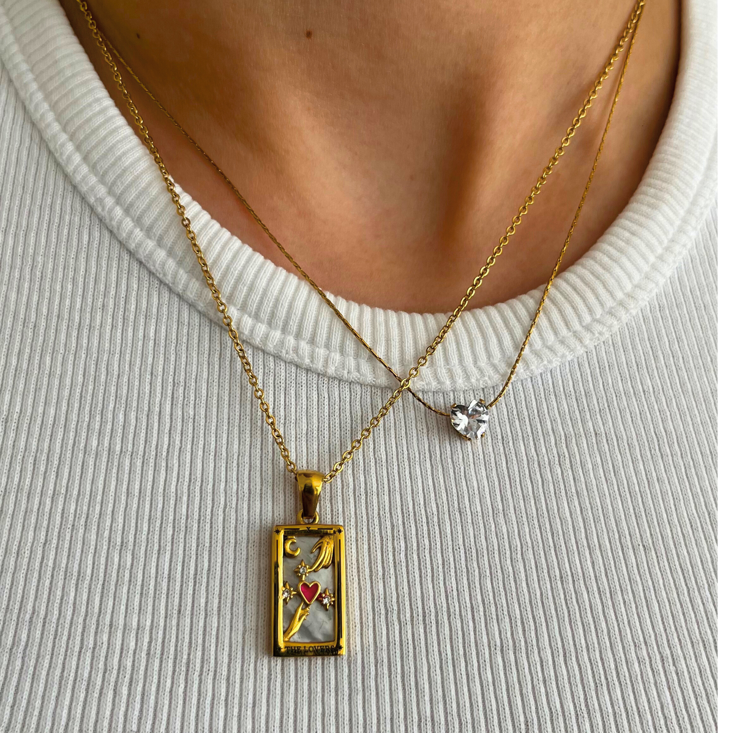 Collar dorado con dije rectangular de carta del tarot “The Lovers”, con detalles de manos, estrellas y corazón rojo.