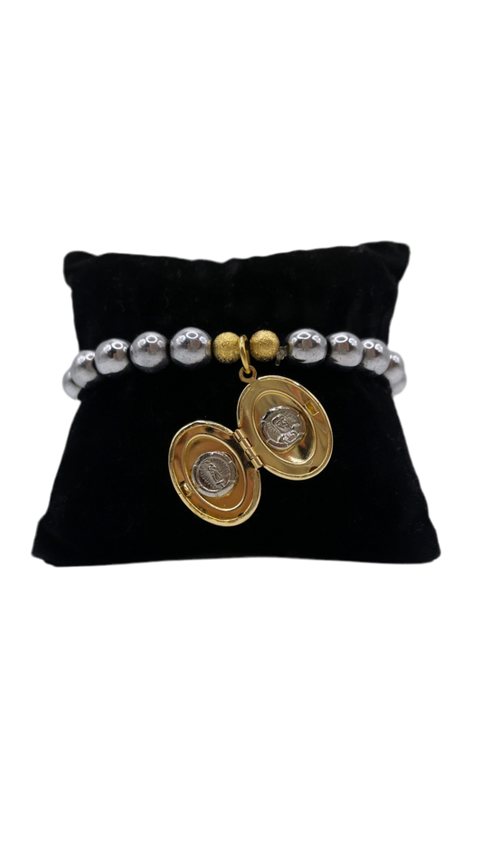 Brazalete elástico con perlas metálicas plateadas y relicario dorado en forma de óvalo, abierto y cerrado. Diseño emocional de bisutería fina.”