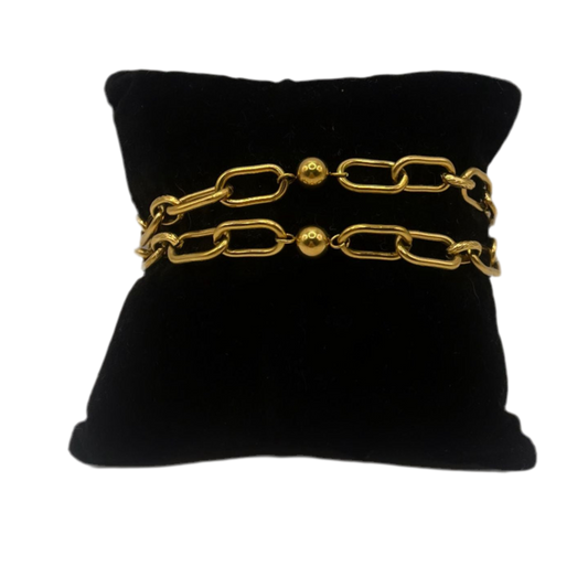“Pulsera dorada de eslabones con esferas decorativas, exhibida sobre cojín negro. Diseño elegante